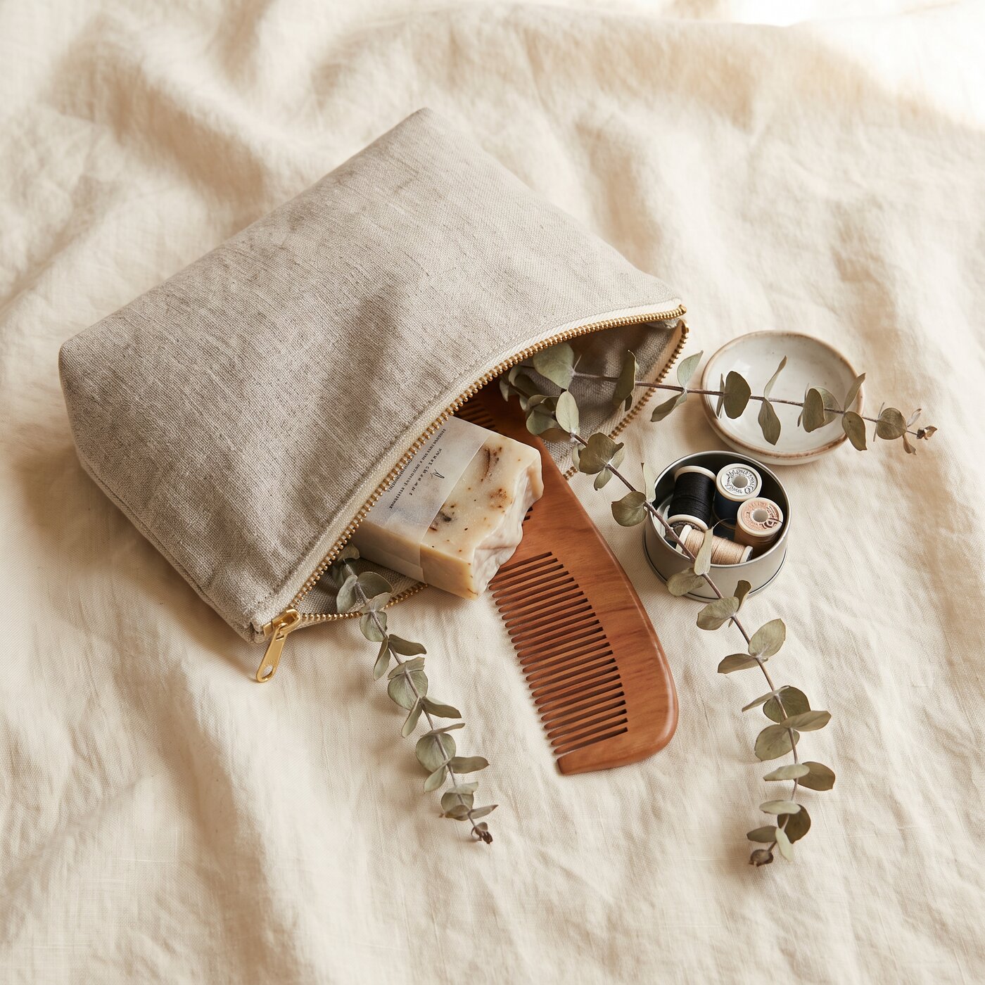 Open linen amenity pouch with soap, comb, and sewing kit